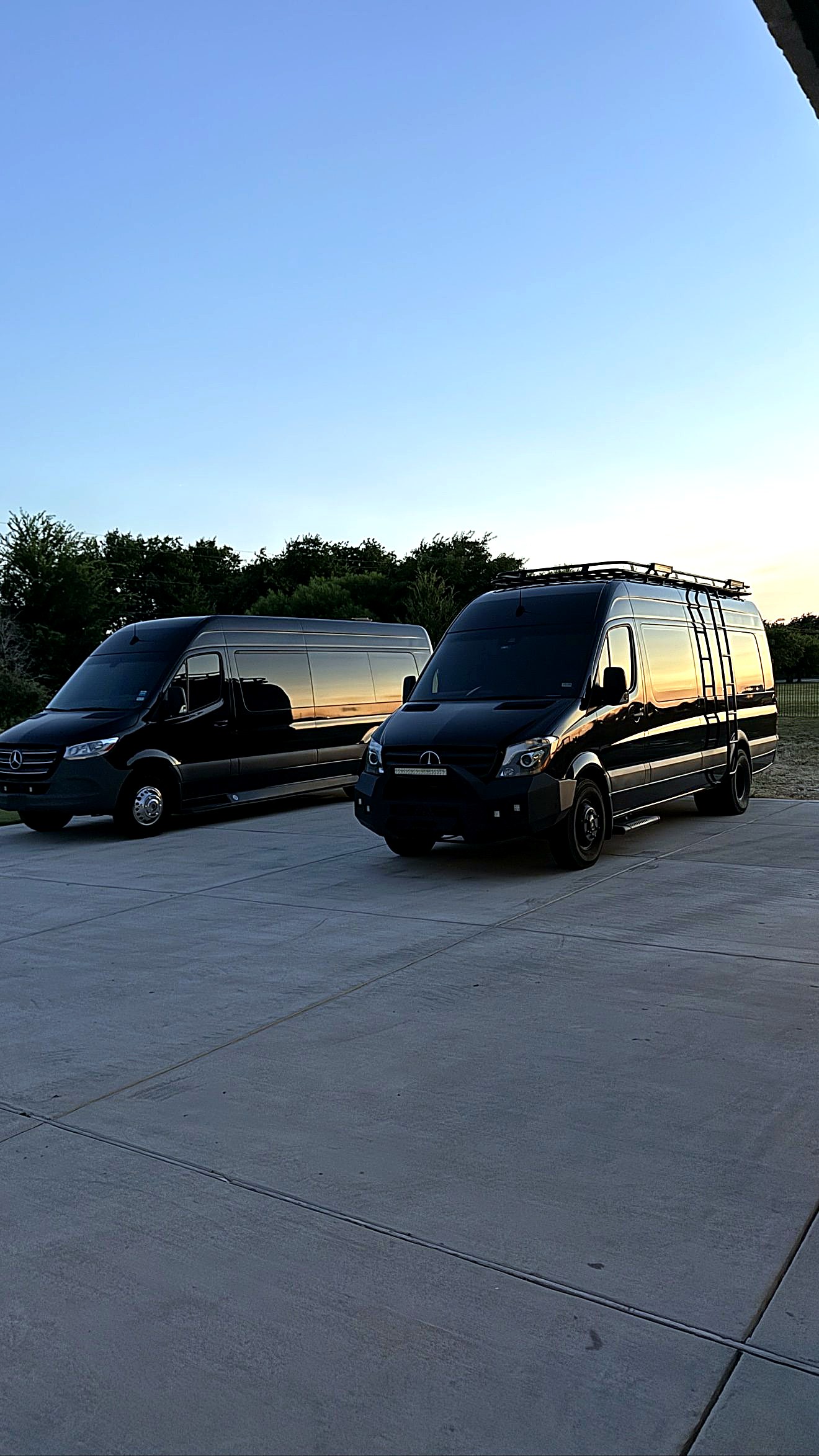 Two black ExecSprinters Mercedes-Benz Sprinters parked side by side at sunset